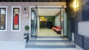 Une entrée moderne avec des portes vitrées, une enseigne indiquant « Avenue Residence », et un espace détente à l’intérieur.