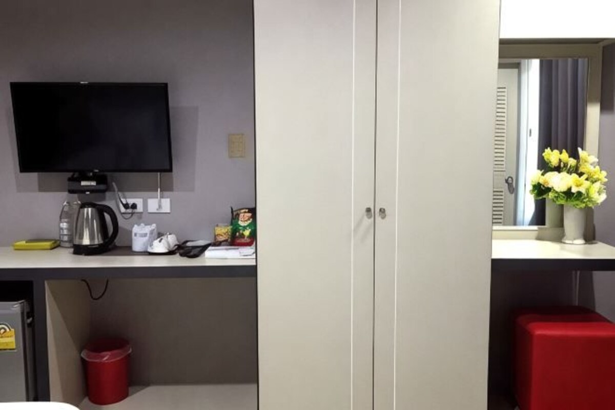Une chambre d’hôtel équipée d’une télévision, d’une petite table avec une machine à café, d’une poubelle rouge et d’un tabouret rouge.