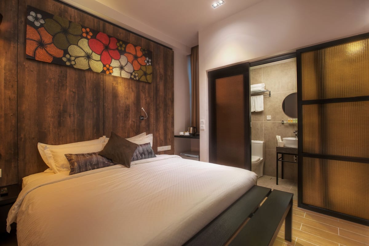 A modern bedroom with a large bed, a wooden headboard, a wall art piece, and a sliding door leading to a bathroom.