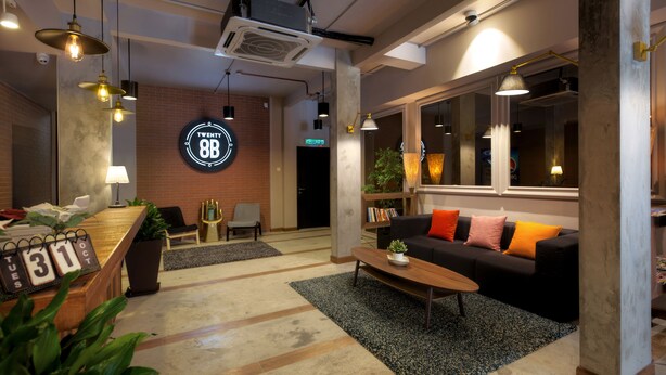 Um lobby moderno com balcão de recepção, um sofá preto com almofadas laranja, uma mesa de centro de madeira e uma janela grande.