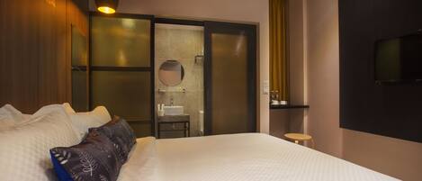 A hotel room with a large bed, a bedside table, a mirror, a small stool, and a TV mounted on the wall.
