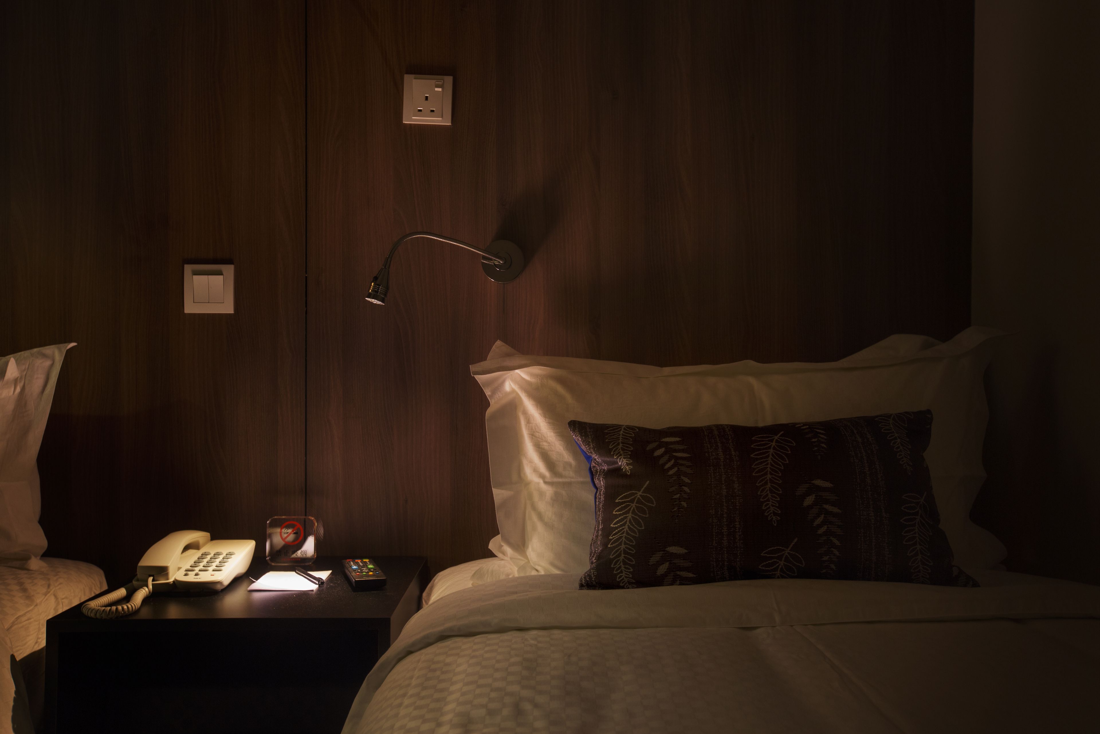A hotel room with a bed, a bedside table with a telephone, a lamp, and a nightstand with a clock.