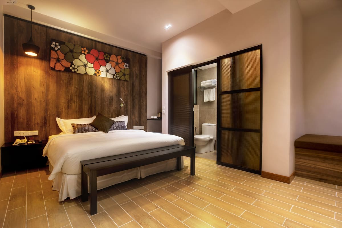 A bedroom with a wooden headboard, a large bed with white bedding, a bedside table with a lamp, and a bench.