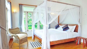Un dormitorio con una cama con dosel, una silla de mimbre y un banco de madera.