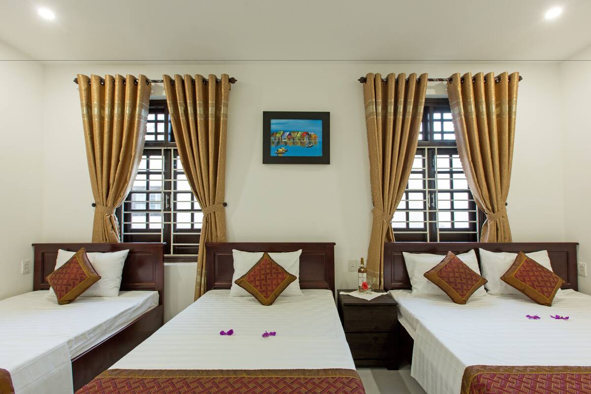 A hotel room with two single beds, a wooden headboard, a nightstand with a bottle and a flower, and a framed picture on the wall.