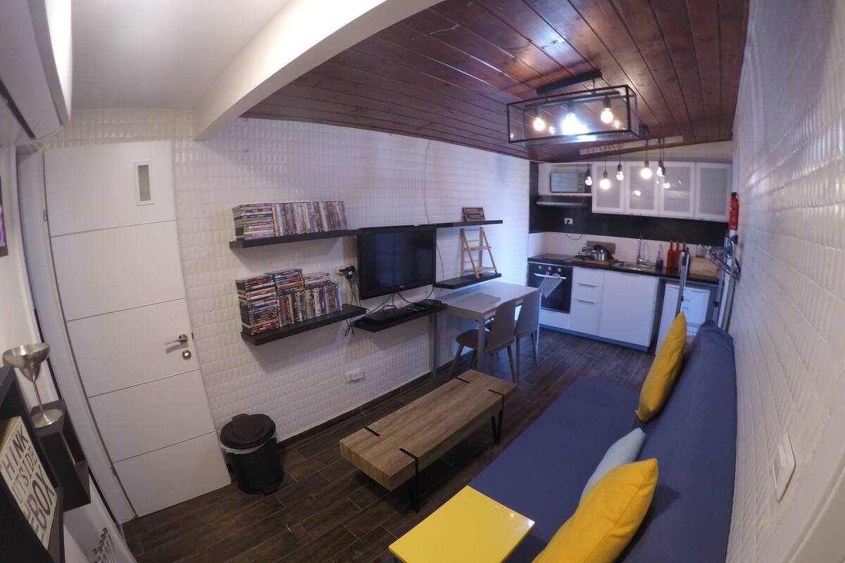 Un espacio habitable compacto con kitchenette, comedor y sofá con cojines.