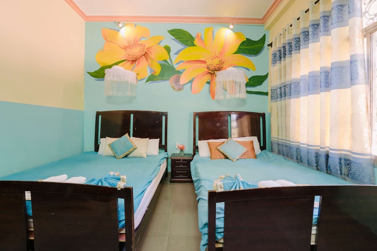 A room with two single beds, a small table with a vase, and a wall mural of flowers.