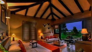 A spacious living room with a high ceiling, a large window offering a view of the outdoors, a fireplace, and a cozy seating area. - Pugdundee Safari- Denwa Backwater Escape (Sohagpur)