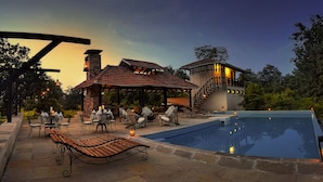 A pool area with lounge chairs, a covered seating area, and a building with a staircase. - Pugdundee Safari- Denwa Backwater Escape (Sohagpur)