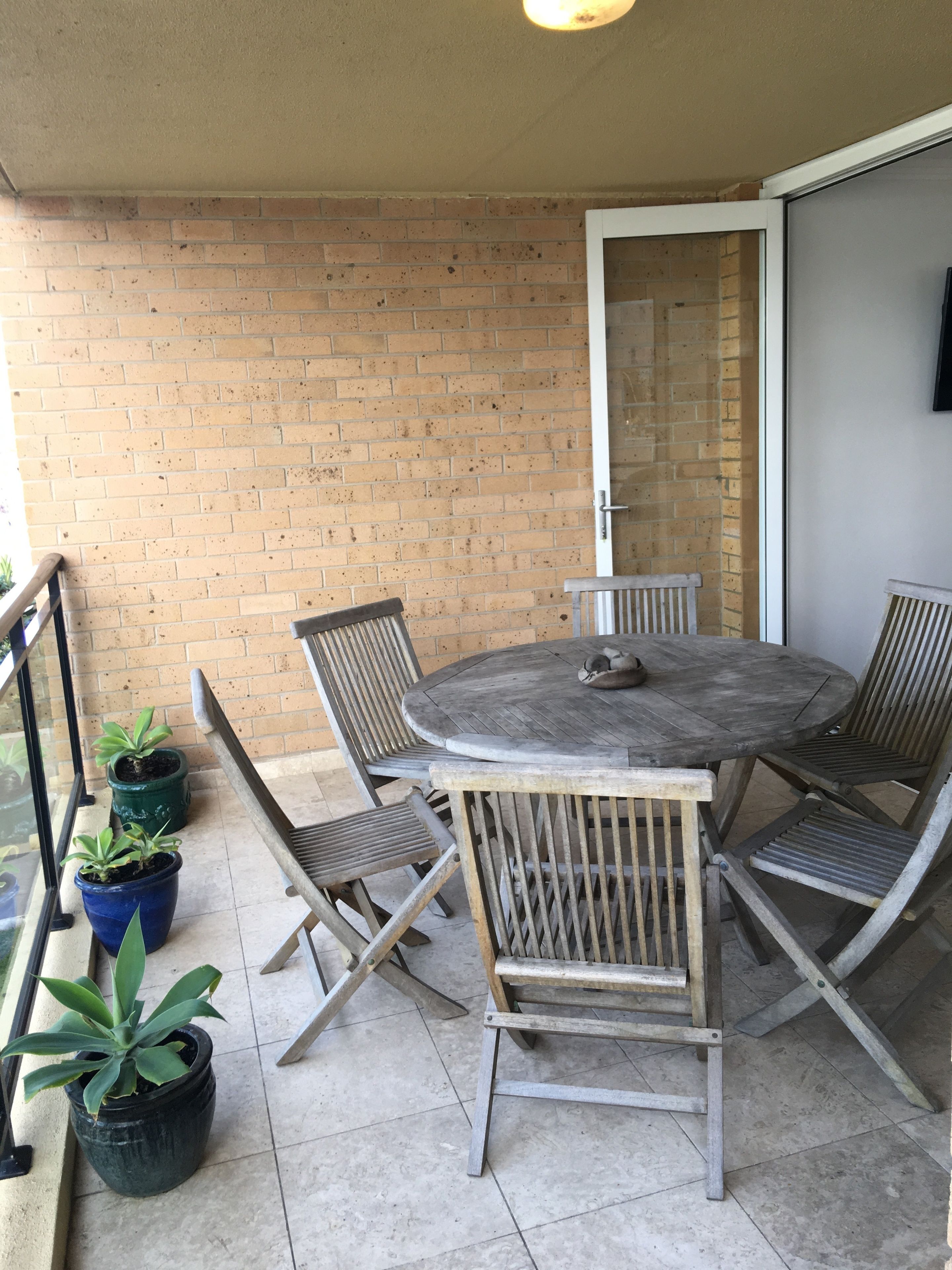 A small outdoor patio with a round table and four chairs, surrounded by potted plants.