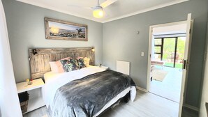 A bedroom with a bed, a ceiling fan, a nightstand, a framed picture on the wall, and a door leading to a balcony. - The Salt House (Cape Town)