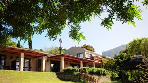 A two-story house with a red roof, a stone wall, and a thatched structure. - The Salt House (Cape Town)