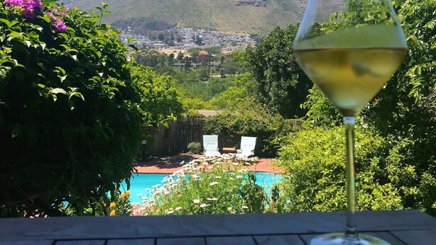 A glass of white wine on a wooden table with a view of a mountain and a pool in the background. - The Salt House (Cape Town)