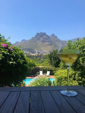 A glass of white wine on a wooden table with a view of a mountain and a pool in the background. - The Salt House (Cape Town)