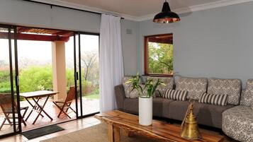A living room with a sofa, a coffee table, a potted plant, and a view of the outdoors.