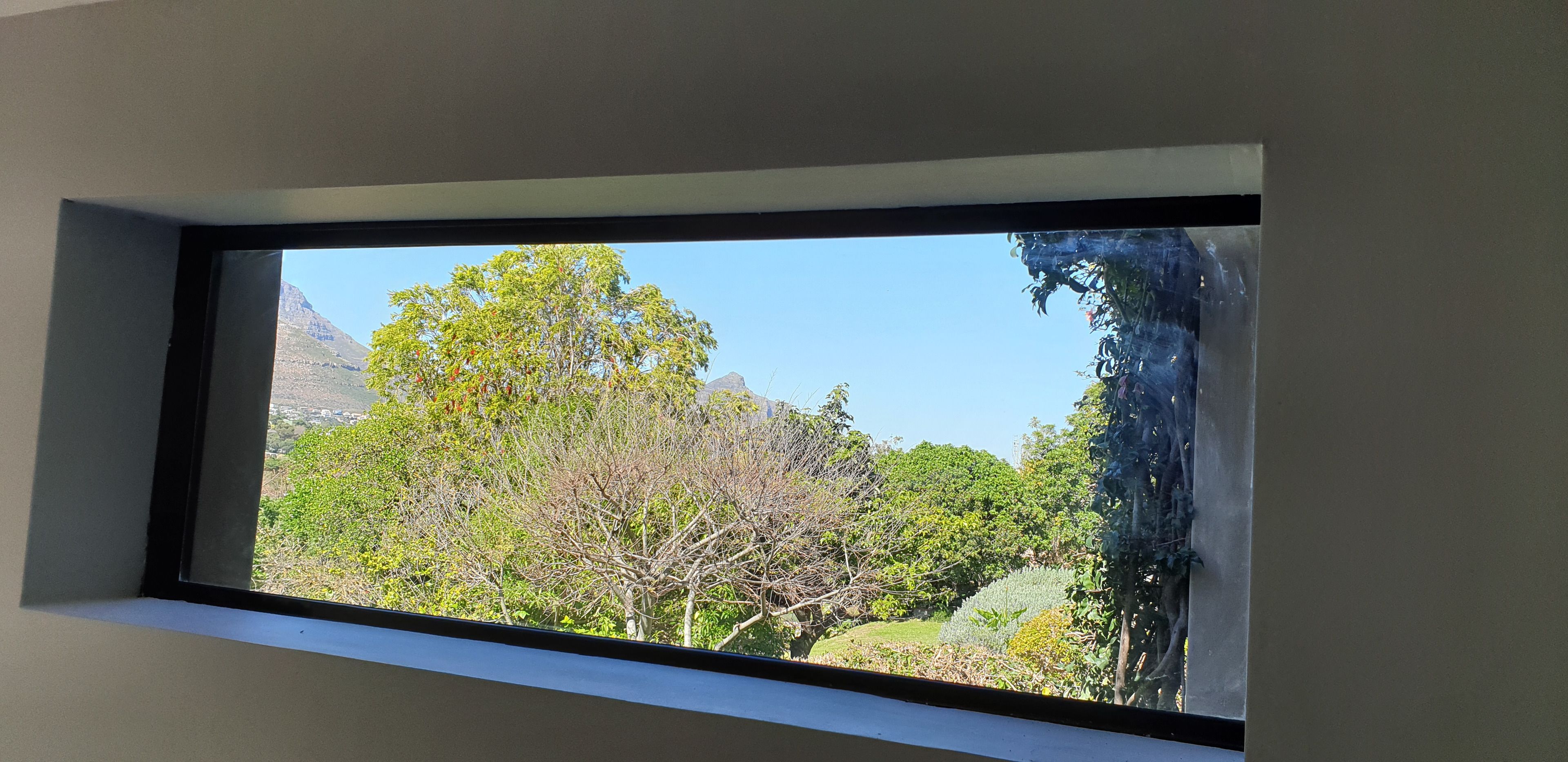 A window with a clear view of a mountainous landscape and dense foliage.