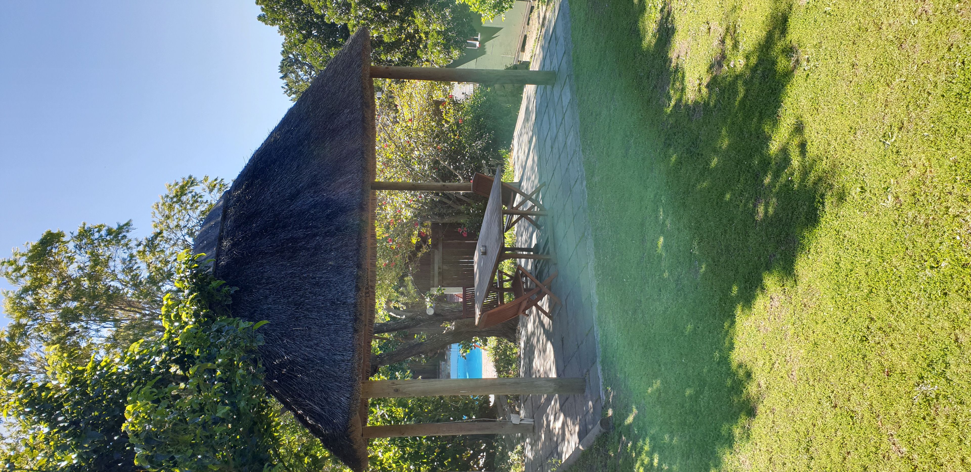 A gazebo with a thatched roof, surrounded by a grassy area and trees.