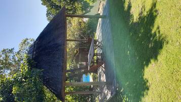 A gazebo with a thatched roof, surrounded by a grassy area and trees.