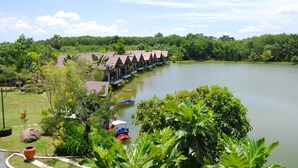 A row of bungalow-style accommodations with a view of a lake and lush greenery. - Tamali Hotel (Phra Phrom)