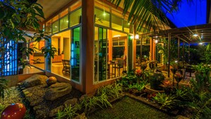 A modern building with large glass windows, outdoor seating, and tropical plants. - Tamali Hotel (Phra Phrom)