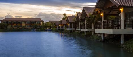 A waterfront hotel with multiple buildings, a calm river, and a sunset sky.