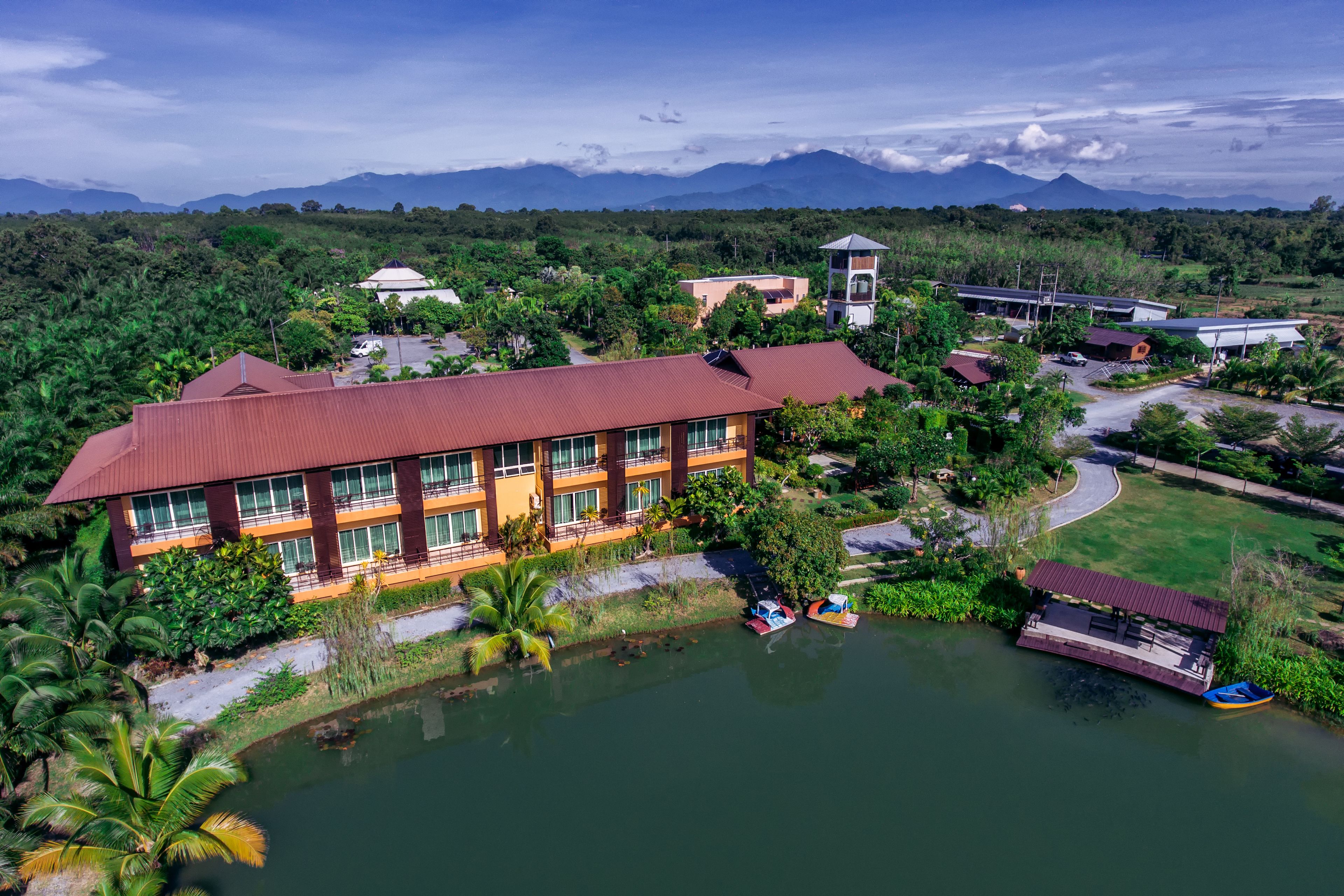 A large building with a red roof, surrounded by greenery and a body of water.
