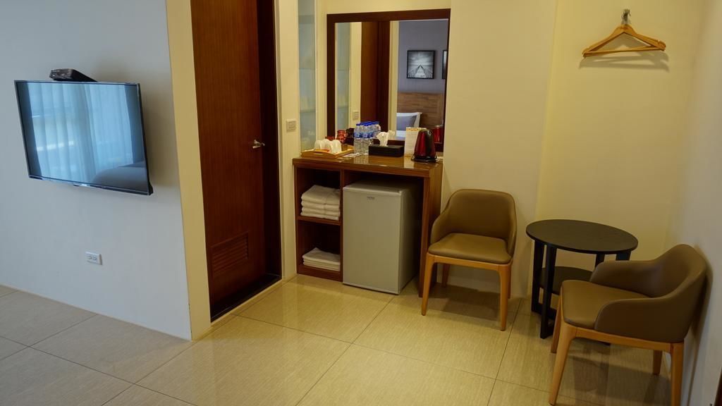 A hotel room with a TV, a desk with a computer, a mini-fridge, two chairs, and a small table.