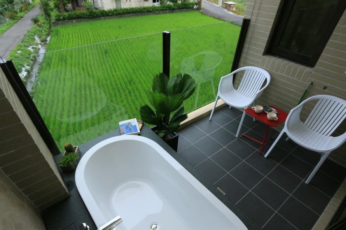 A balcony with a white bathtub, two white chairs, and a small table with a book and a plant.