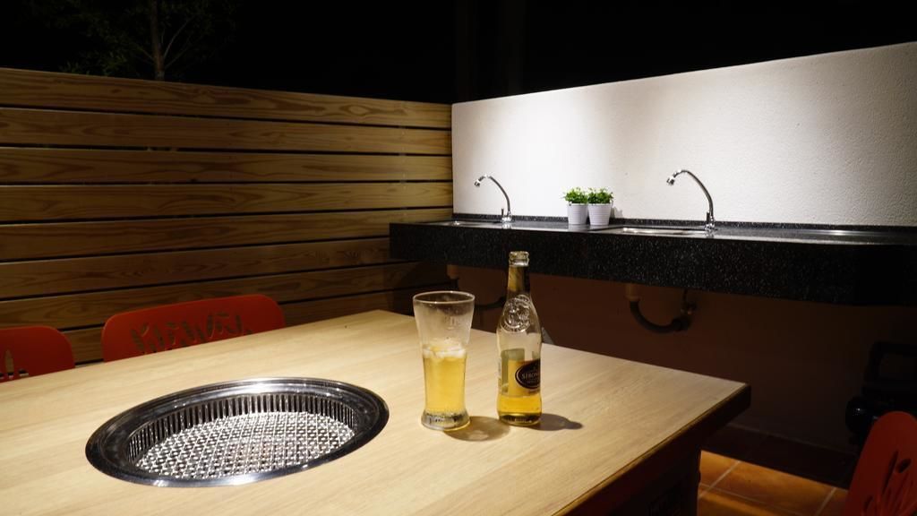 A wooden table with a glass and bottle, a metal tray, and a black countertop with a sink and potted plants.