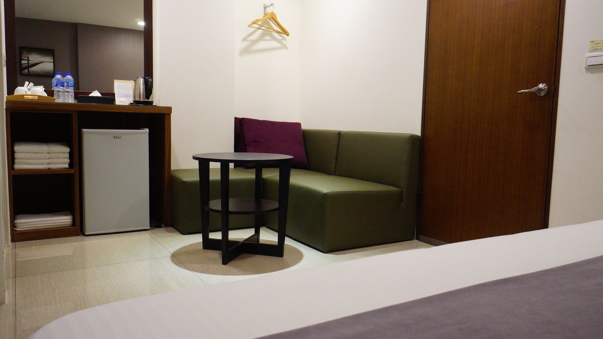 Habitación de hotel compacta con cama, una mesita, sofá verde, armario y un mini refrigerador.