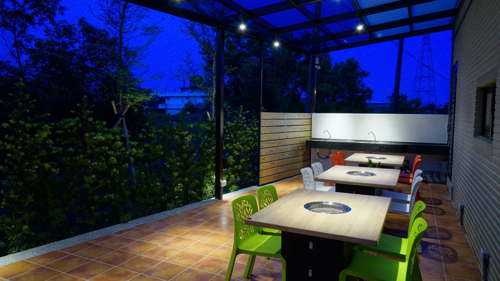 An outdoor patio with a wooden table and chairs, a built-in grill, and a view of the surrounding greenery.
