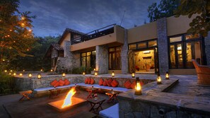 Un espacio de estar moderno al aire libre, con muros de piedra, chimenea y una iluminación ambiental.