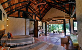 Una habitación acogedora con techo de madera alto, una cama con manta a rayas, una pequeña mesa con sillas y vistas al exterior.