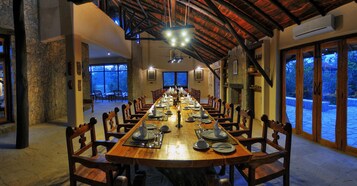 Una larga mesa de comedor dispuesta para una comida en una habitación amplia con paredes de piedra y vigas de madera.