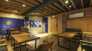 A restaurant interior with wooden tables and chairs, a dartboard, and a television screen displaying a sports event. - Twelve Motel (Chilgok)