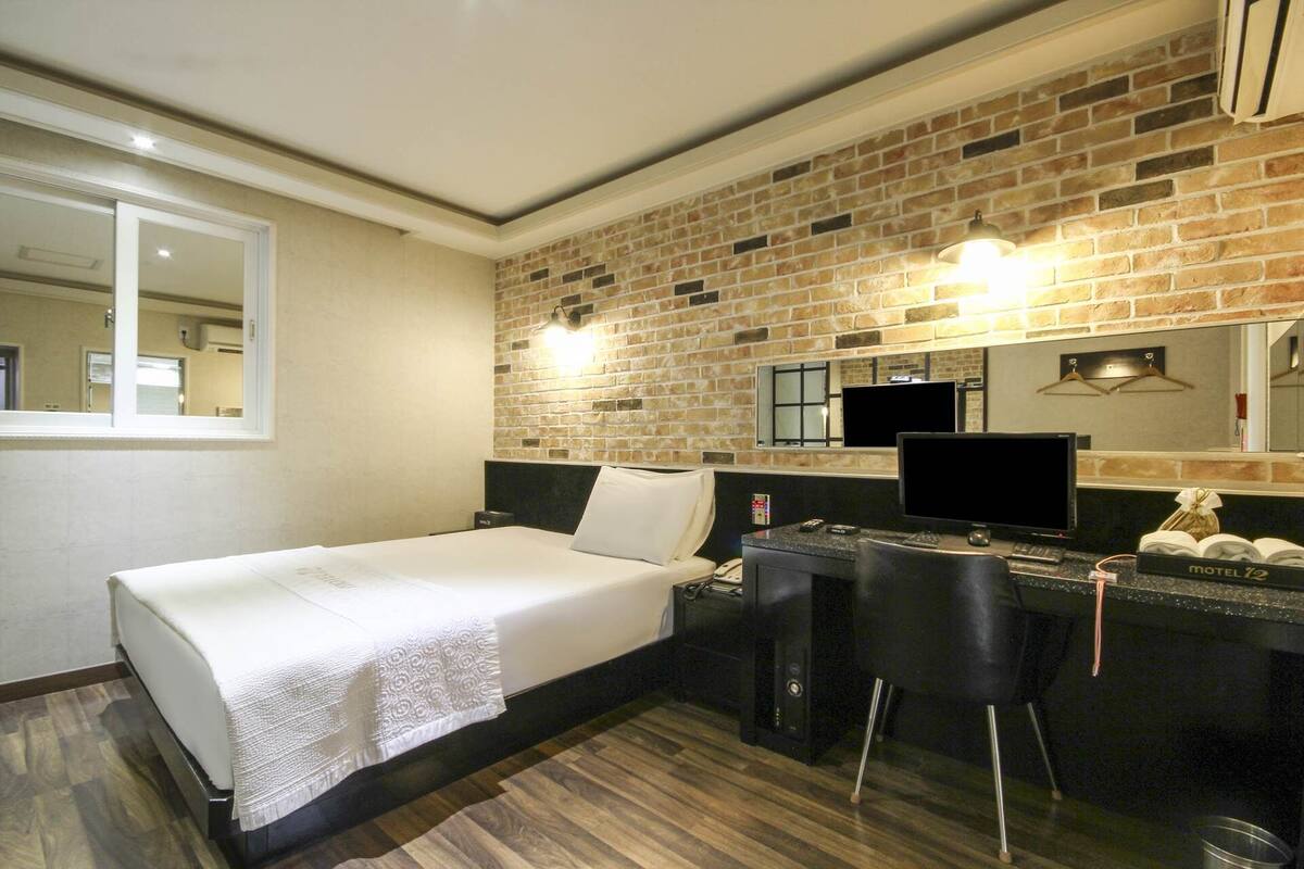 A hotel room with a bed, a desk, a chair, a TV, and a brick wall.