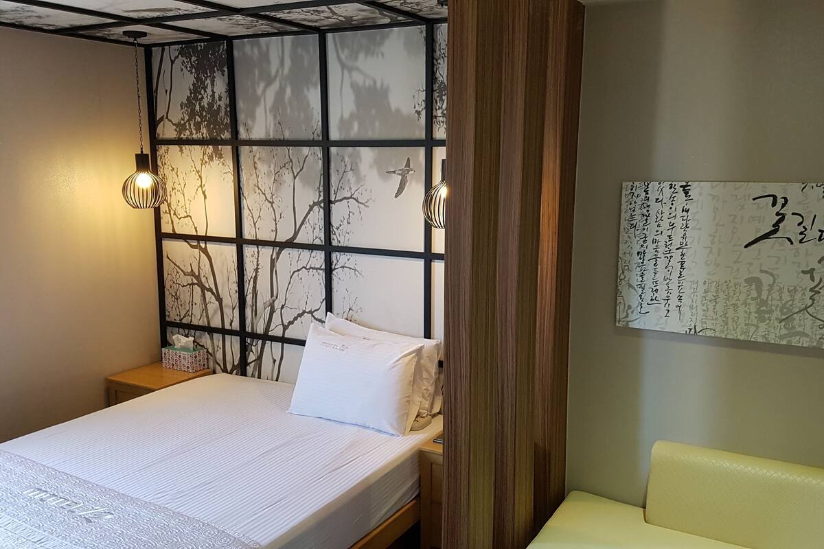 A bedroom with a bed, a nightstand, a wall-mounted shelf, and a bedside table.