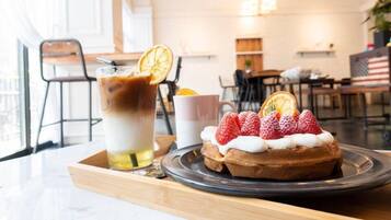Una bandeja con postres, una gofre, fresas y una bebida sobre una mesa de madera en una cafetería.