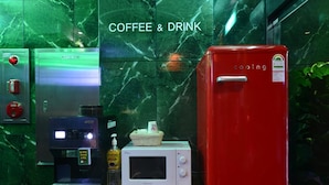 Eine Kaffeemaschine, eine Mikrowelle und ein roter Kühlschrank in einer Küchenzeile mit Marmorrückwand.