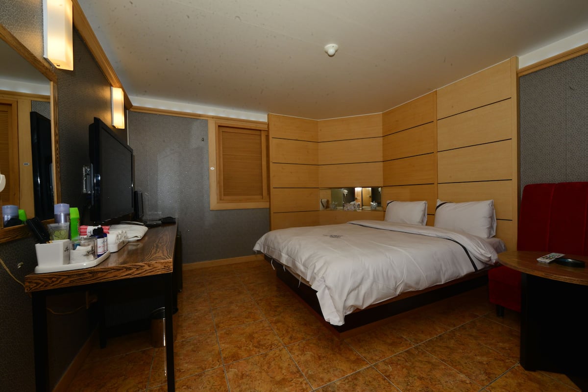 Ein Hotelzimmer mit einem Bett, einem Schreibtisch mit Spiegel, einem roten Sessel und einem kleinen Tisch.
