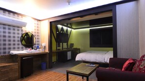 Ein kleines Hotelzimmer mit Bett, Schreibtisch, Spiegel und einem roten Sofa.