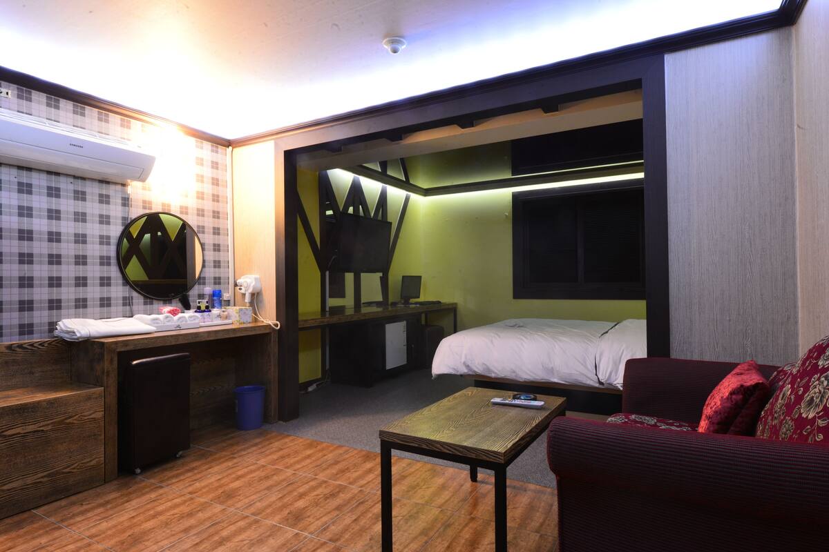 Ein kleines Hotelzimmer mit Bett, Schreibtisch, Spiegel und einem roten Sofa.