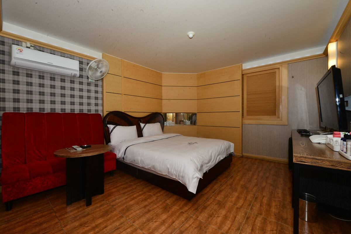 Ein Schlafzimmer mit einem Bett, einem roten Sofa, einem kleinen Tisch, einem Fernseher und einer Klimaanlage.
