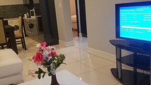 A modern living room with a white coffee table, a vase with flowers, a remote control, and a television displaying an OTA upgrade screen. - 77 On Independence Windhoek (Windhoek)