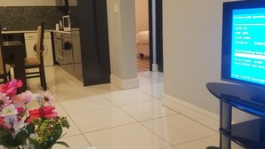 A modern living room with a flat-screen TV displaying a download screen, a dining area with a vase of flowers, and a kitchen in the background. - 77 On Independence Windhoek (Windhoek)