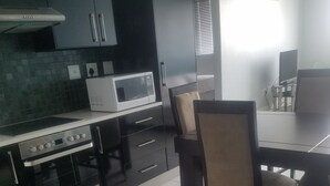 A modern kitchen with a stove, microwave, and dining area with chairs. - 77 On Independence Windhoek (Windhoek)