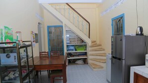 A compact kitchen with a dining table, chairs, a refrigerator, and a staircase leading to an upper level. - Memory Vintage Home Da Lat (Cam Ly - Da Lat)