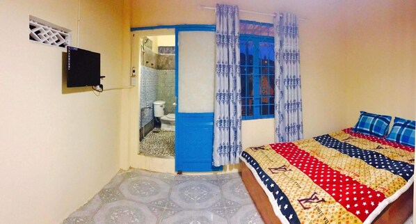 A bedroom with a bed, a bathroom, and a window with curtains.