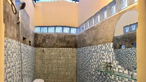 A small bathroom with a toilet, sink, and shower. The walls are tiled with blue and gray mosaic tiles. - Memory Vintage Home Da Lat (Cam Ly - Da Lat)