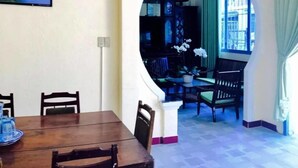 A dining area with a wooden table and chairs, a framed picture on the wall, and an archway leading to a seating area with a view of the outside. - Memory Vintage Home Da Lat (Cam Ly - Da Lat)